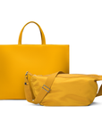 The saffron tote bag with a removable, adjustable shoulder strap and a matching mini sling bag. The larger tote has a snap closure and zippered pockets, while the smaller sling has an adjustable strap.