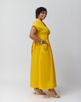 A model showing the side of the wrap dress in marigold. Details of the front pockets are showing as well on a neutral background.