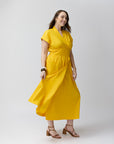 A model smiling, wearing the marigold warp dress with heels.