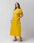 A model positioned on the side, wearing the wrap dress in marigold. She has her hand on one of the front pockets of the dress.