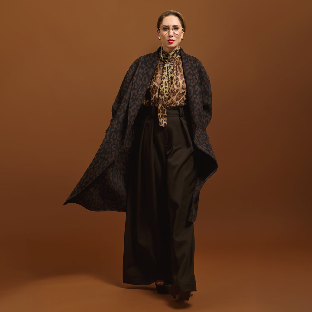 Woman wearing the Leopard Jacquard coat, patterned shirt, and black pants on a brown background.