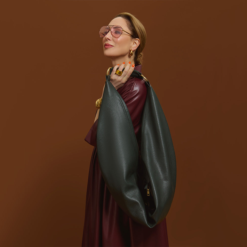 Carla holding the Bottle Green Sling Bag on a brown background.