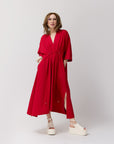 A model wearing a red maxi shirt dress with three quarter sleeves, side slits, and a deep V-neck. The dress features a high waist with drawstring details.