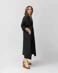 Side view of Carla modeling the shirt dress in black, showing the silhouette and mid-calf hem, with her gold platform sandals.