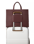 2-in-1 Tote Bag in Cherry Cola luggage sleeve on a white suitcase.