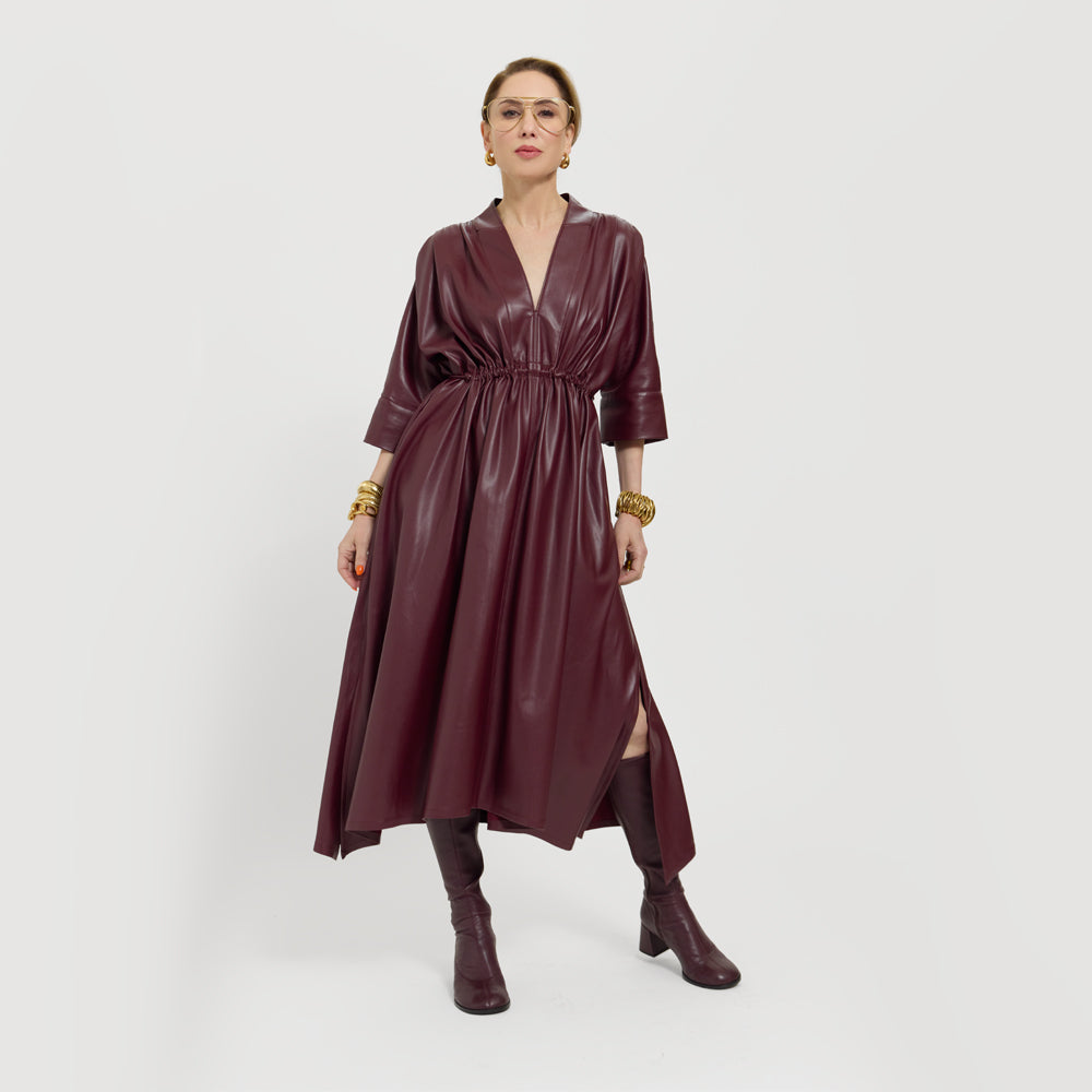 Carla is wearing the vegan leather dress in Merlot on a plain background.