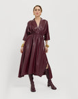 Carla is wearing the vegan leather dress in Merlot on a plain background.
