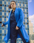 Model with the cobalt coat standing in front of a cityscape with a blue sky.