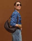 Carla holding the Mini Sling Bag in Chocolate against a brown background.