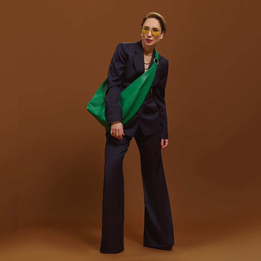 Carla modeling the Sling Bag in Emerald Green on a brown backgroung.