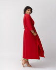 Side view of the model in the poppy red shirt dress, emphasizing the mid-calf length and soft jersey fabric, with heels visible against a simple studio background.