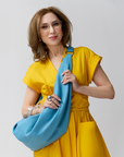 Carla Rockmore is modeling the Sling Bag 2.0 in Sky Blue as a crossbody bag. She is wearing the Wrap Dress in Marigold.