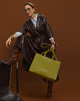 Carla modeling the Avocado Tote bag in the vegan leather dress against a brown background.