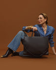 Carla sitting on the floor with a 2-in-1 Tote Bag in black handbag against a brown background.