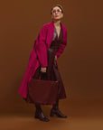 Carla modeling the Cherry Cola Tote Bag and the coat is Orchid on a brown background.