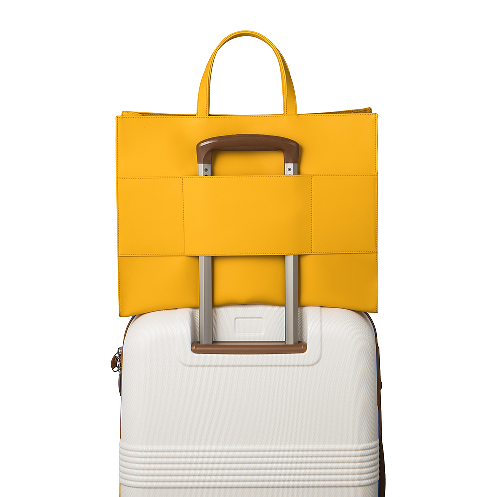 The saffron tote bag on top of a  luggage using the luggage sleeve feature on the back of the bag that allows for convenient attachment to luggage.