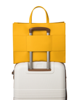 The saffron tote bag on top of a luggage using the luggage sleeve feature on the back of the bag that allows for convenient attachment to luggage.
