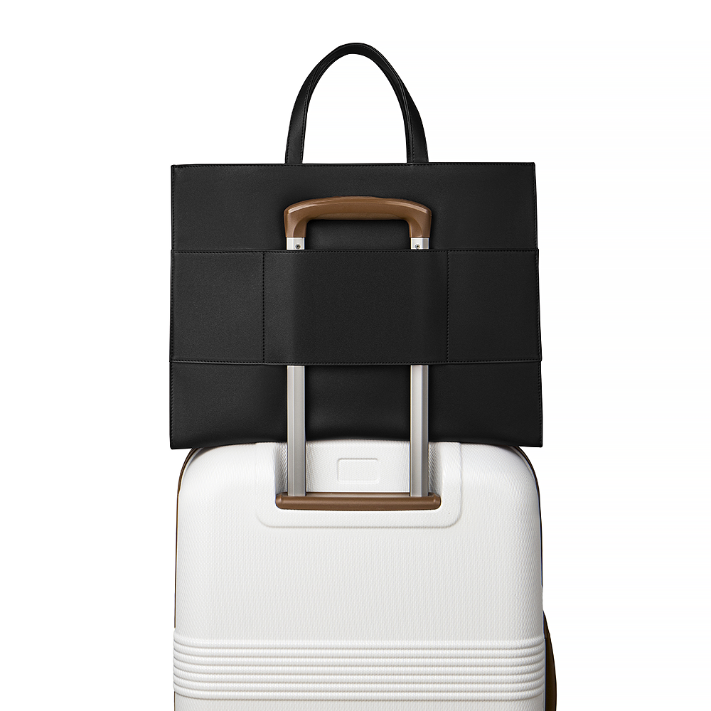 2-in-1 Tote Bag in Black showing the travel sleeve luggage on a white suitcase.