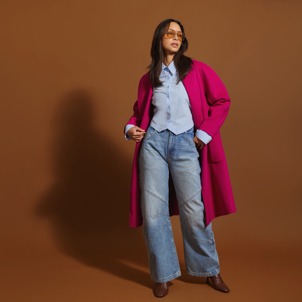 Woman wearing the orchid coat, light blue jeans, and sunglasses on a brown background.