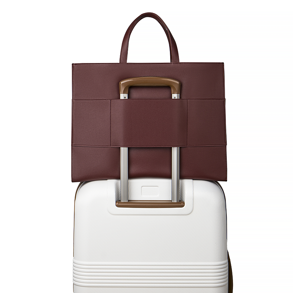 2-in-1 Tote Bag in Cherry Cola luggage sleeve on a white suitcase.