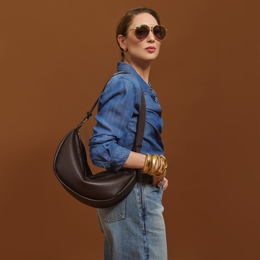 Carla holding the Mini Sling Bag in Chocolate against a brown background.