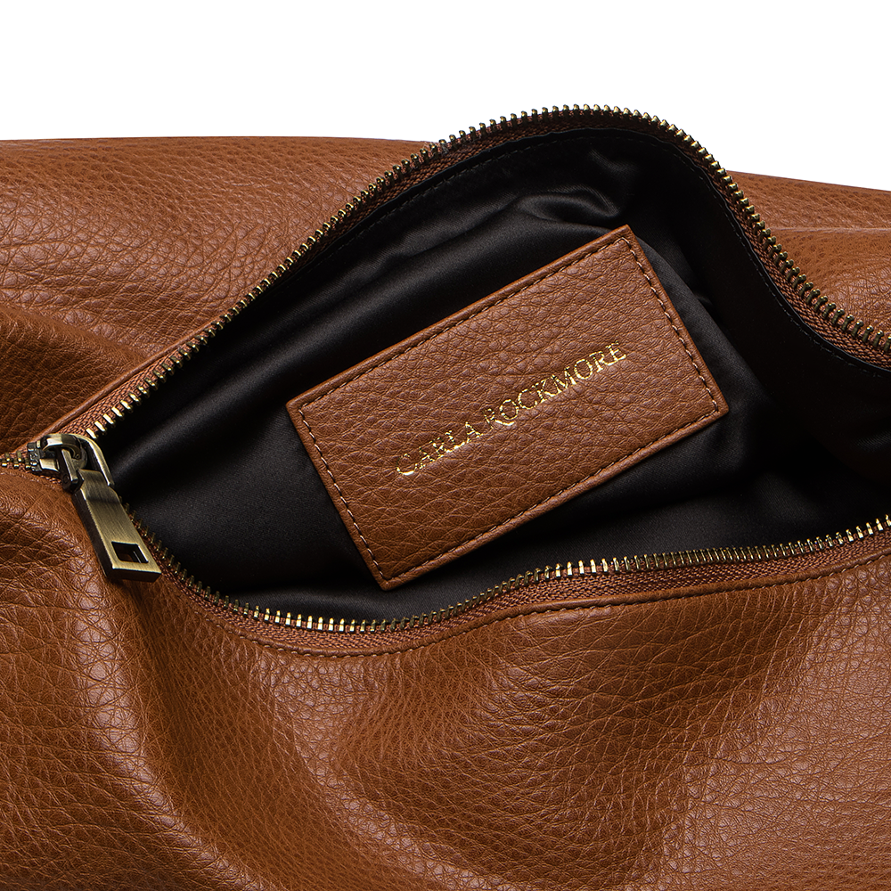 Close-up of the Sling Bag in Saddle with a visible brand label on a white background.
