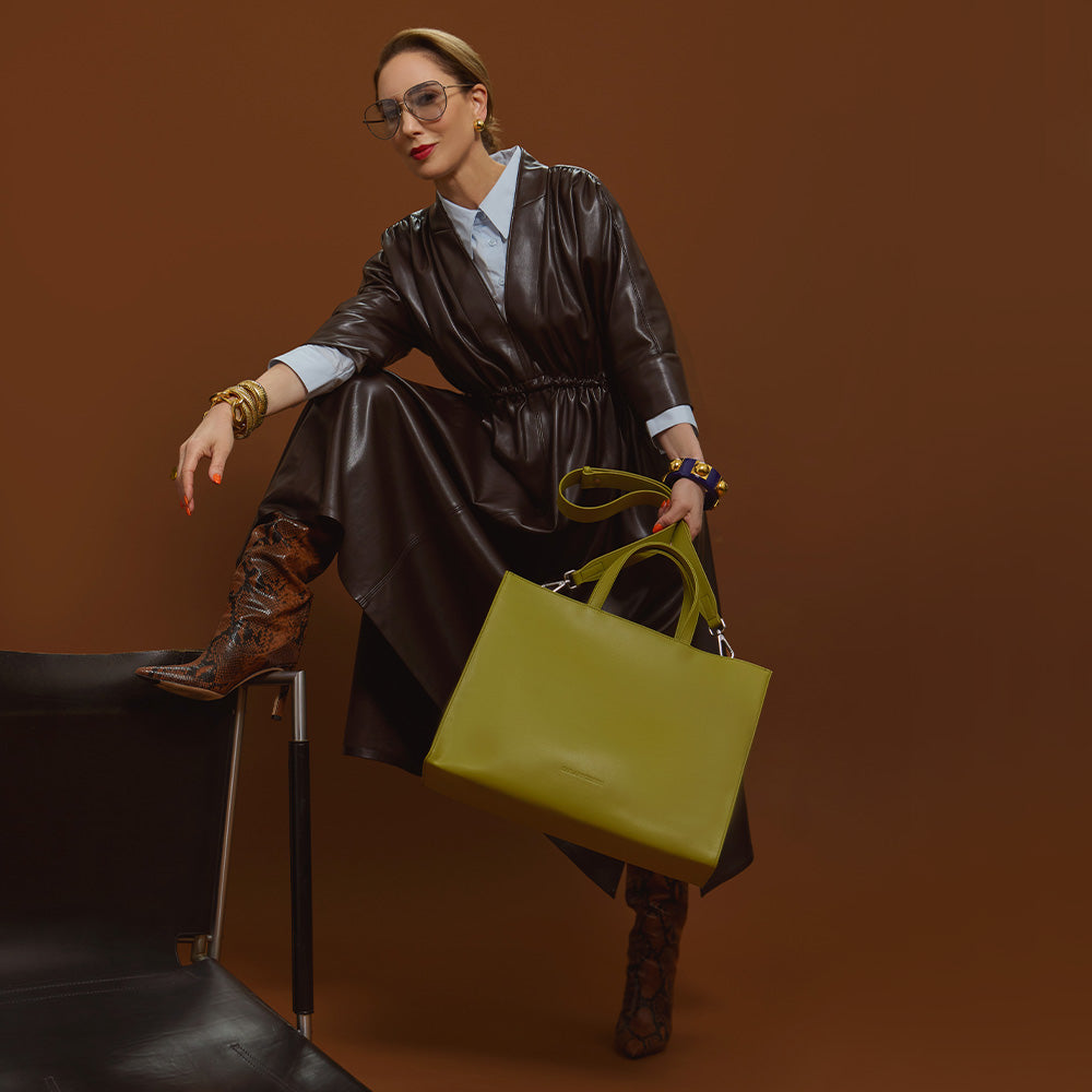 Carla modeling the Avocado Tote bag in the vegan leather dress against a brown background.