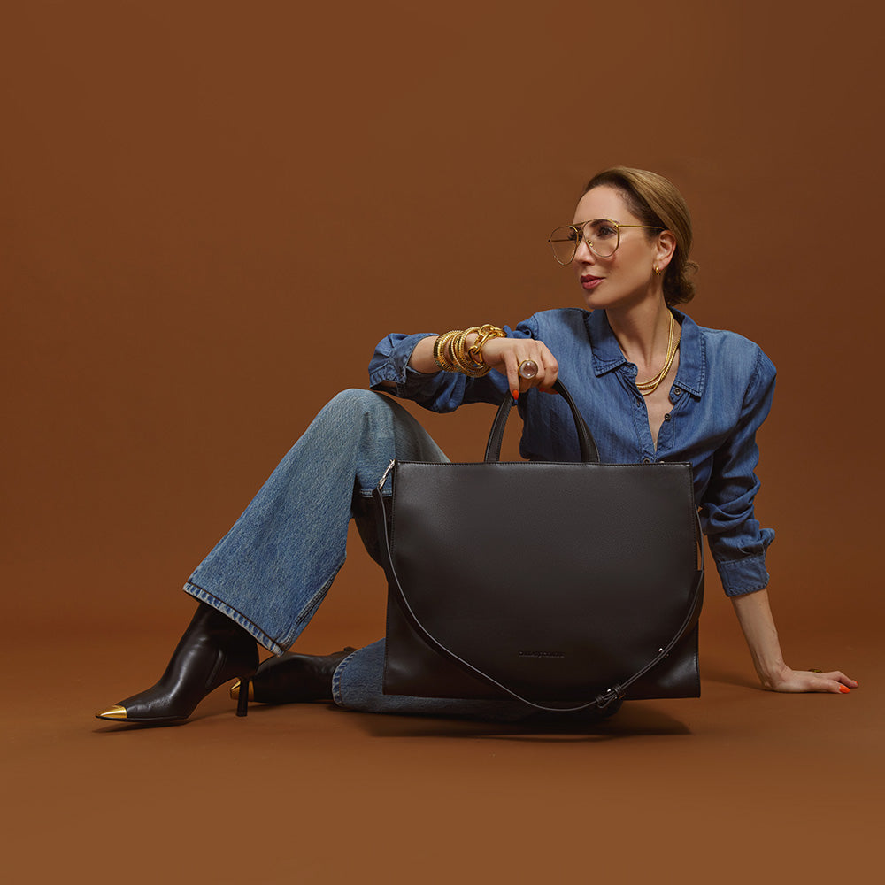 Carla sitting on the floor with a 2-in-1 Tote Bag in black handbag against a brown background.